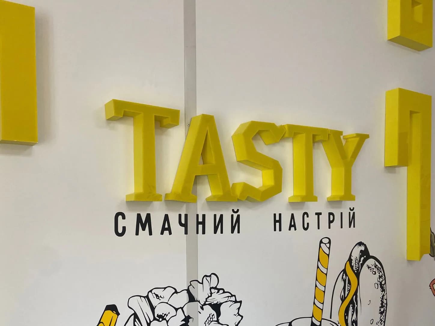 Жовта інтер’єрна вивіска Tasty на оформленій стіні закладу