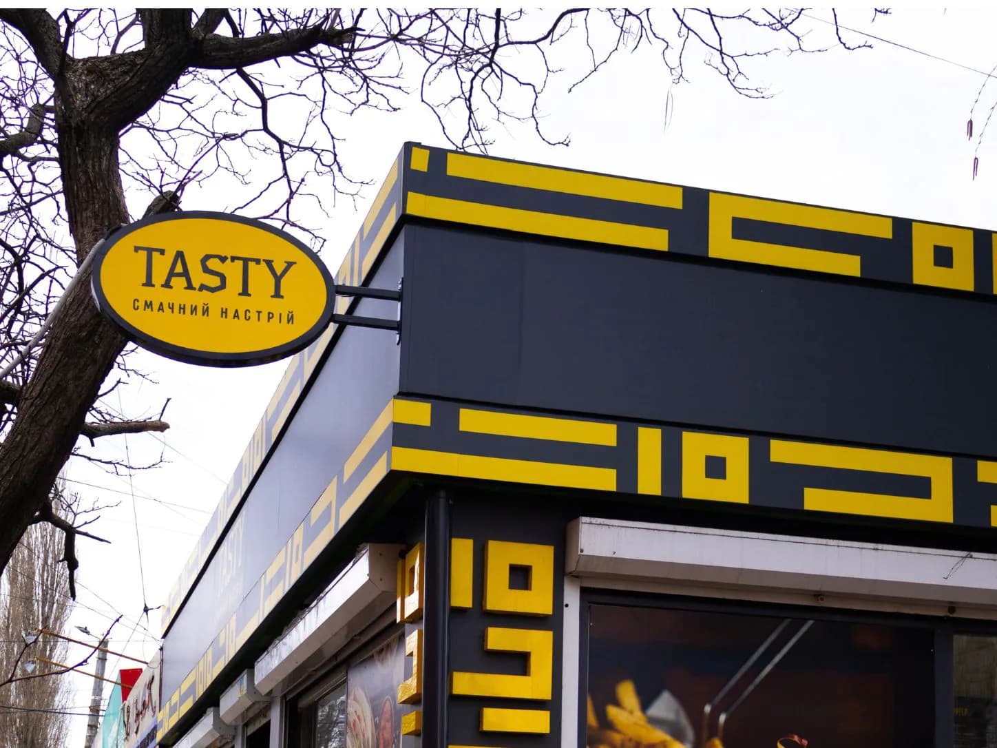 Овальна консольна вивіска Tasty на куті фасаду