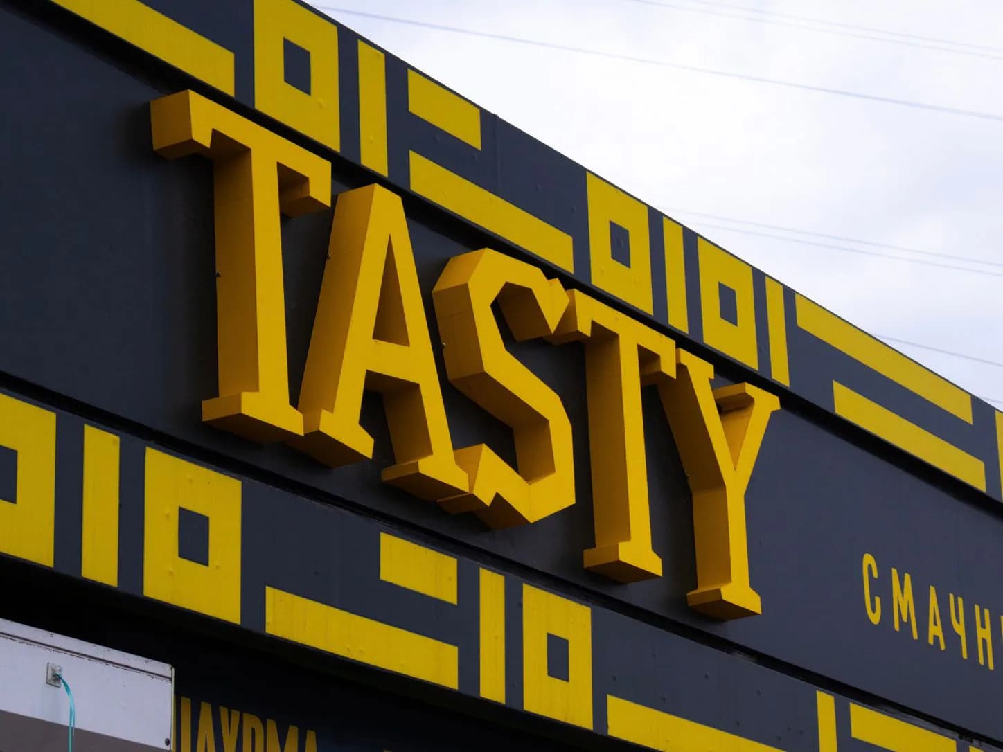 Жовті об’ємні літери Tasty на темній фасадній панелі