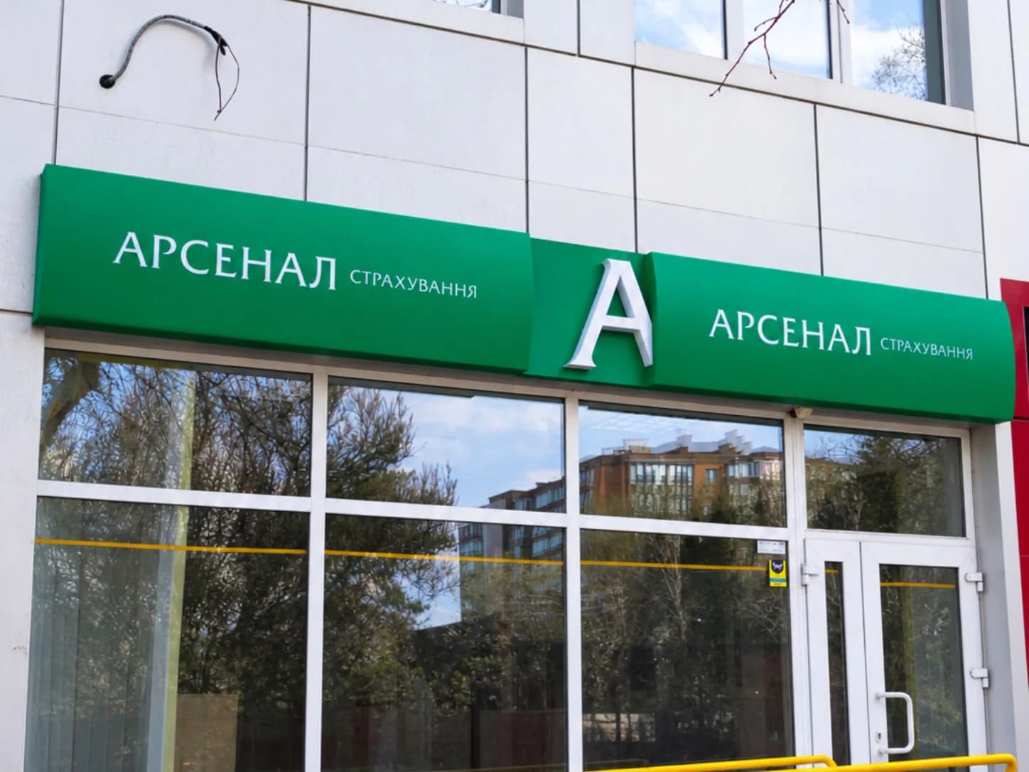Фасад «Арсенал Страхування» із зеленою вивіскою, білою літерою «А» та входом із пандусом.