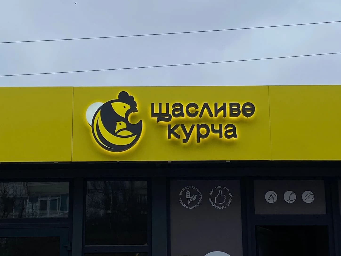 Фронтальний фасад магазину «Щасливе курча» з об’ємною світловою вивіскою та входом
